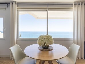 Ein runder Tisch mit einer Blumenvase, zwei Stühlen und Meerblick durch große Fenster.