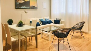 Een moderne woonkamer met een witte bank, blauwe kussens, een glazen salontafel en zwarte rieten stoelen.