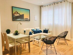 Ein modernes Wohnzimmer mit einem weißen Sofa, blauen Kissen, einem Glastisch und schwarzen Korbstühlen.