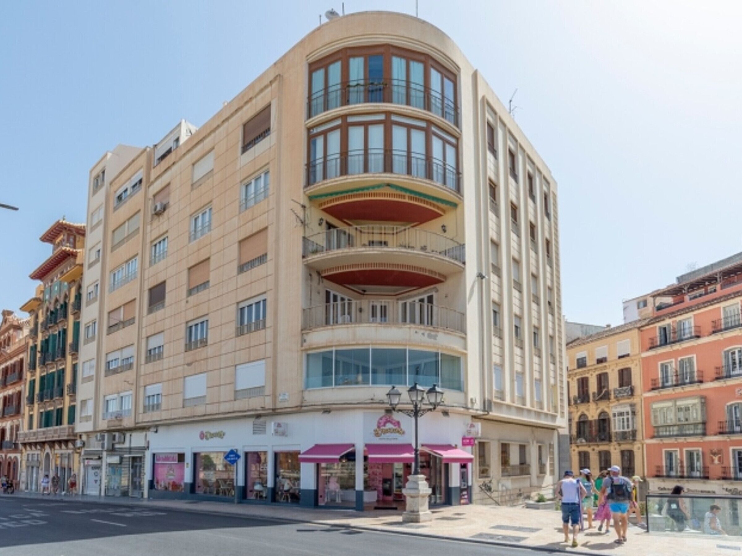 Un hôtel à plusieurs étages, doté d’une façade incurvée sur un coin, de grandes fenêtres et d’un magasin situé au rez-de-chaussée.