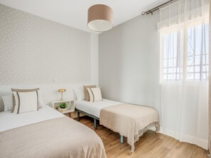 A bedroom with two beds, a bedside table with a lamp, and a window with curtains. - Torremolinos: Family relaxation with a lovely terrace. (Torremolinos)