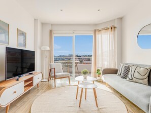 Un salon moderne doté d’un téléviseur à écran plat, d’un canapé, d’une table à manger et offrant une vue sur la ville grâce à de grandes fenêtres.