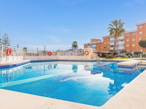 A swimming pool with a tiled edge, a white fence, and palm trees in the background. - Torremolinos: Family relaxation with a lovely terrace. (Torremolinos)