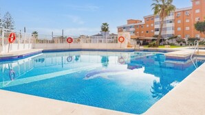 A swimming pool with a white fence and lifebuoys, surrounded by palm trees and a multi-story building. - Torremolinos: Family relaxation with a lovely terrace. (Torremolinos)