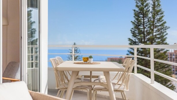 A balcony with a table and chairs, overlooking a clear sky and a distant view of trees and buildings. - Torremolinos: Family relaxation with a lovely terrace. (Torremolinos)