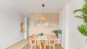 A modern dining area with a wooden table and wicker chairs, a hanging light fixture, and a small plant on a side table. - Torremolinos: Family relaxation with a lovely terrace. (Torremolinos)