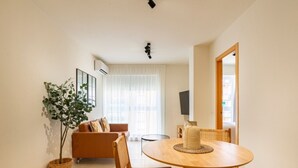 Uma sala de estar moderna com uma mesa de jantar redonda de madeira, cadeiras de vime, um sofá e um vaso com planta.