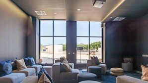 Un'accogliente hall di un hotel moderno, con una grande finestra, comodi posti a sedere e un proiettore a soffitto.