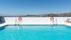 Una piscina sul tetto con acqua cristallina, due galleggianti di salvataggio e vista su dolci colline in lontananza.