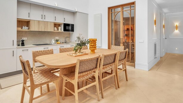 A modern kitchen with white cabinets, a wooden dining table, and wicker chairs. - Exclusive Apartment in Malaga, Near Beach (Málaga)