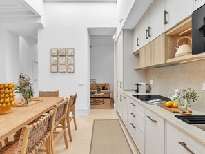 A modern kitchen with white cabinetry, a wooden dining table, and a kitchen island. - Exclusive Apartment in Malaga, Near Beach (Málaga)