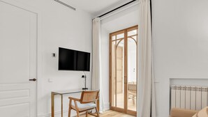A modern living room with a glass desk, a TV mounted on the wall, a wooden chair, a sofa, and a sliding glass door leading to an outdoor area. - Exclusive Apartment in Malaga, Near Beach (Málaga)
