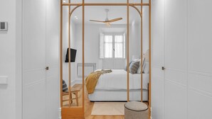 A bedroom with a bed, a wooden partition, a ceiling fan, a radiator, and a small round ottoman. - Exclusive Apartment in Malaga, Near Beach (Málaga)