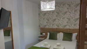 Ein Hotelzimmer mit Bett, Nachttisch, Spiegel und einem an der Wand befestigten Fernseher.