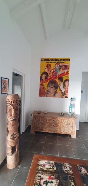 A room with a wooden cabinet, a poster on the wall, and a carved wooden sculpture. - Villa Melodie a grande Anse Deshaies (Deshaies)