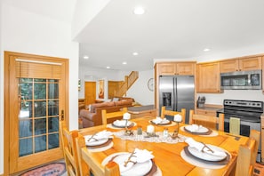 Un comedor con una mesa de madera dispuesta para cuatro personas, un refrigerador y una estufa en la cocina.