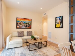 Een woonkamer met een witte bank, een salontafel en twee schilderijen aan de muur.
