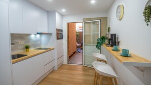 Eine moderne Küche mit weißen Schränken, einer Holz Arbeitsplatte und einem eingebauten Backofen. Es gibt einen kleinen Essbereich mit zwei weißen Stühlen und einer Kaffeemaschine.