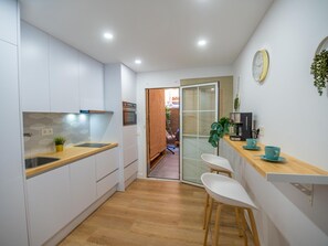 Eine moderne Küche mit weißen Schränken, einer Holz Arbeitsplatte und einem eingebauten Backofen. Es gibt einen kleinen Essbereich mit zwei weißen Stühlen und einer Kaffeemaschine.