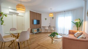 Ein modernes Wohnzimmer mit einem Glastisch, zwei Sofas und einem Fernseher, der an einer Wand aus Holzpaneelen befestigt ist.
