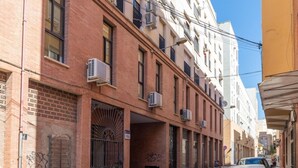 Een smalle stadstraat met een rij gebouwen, herkenbaar aan bakstenen gevels en meerdere airconditioners.