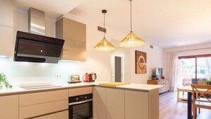 A modern kitchen with a built-in oven, a toaster, and a coffee maker on the counter. There is a dining area with a wooden table and chairs. - Elegant Marbella Apartment with Direct Pool Access and Parking (Marbella)