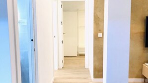 Een hal met houten vloer en witte muren, die leidt naar een kamer met een beige accentmuur en een wandtelevisie.