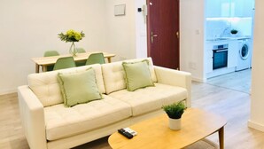 Een woonkamer met een bank, een salontafel, een afstandsbediening en een eethoek met stoelen en een tafel.