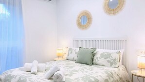 Een hotelkamer met een bed, twee spiegelwanden, een bedlamp en een raam met gordijnen.