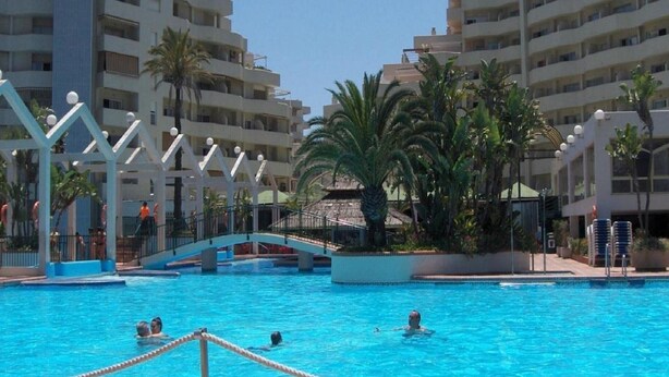 A swimming pool surrounded by multi-story buildings, palm trees, and a bridge. - Seafront apartment with pool in Benalmádena (Benalmádena)