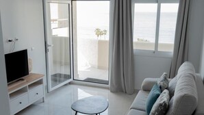 A modern living room with a sofa, a small table, a TV, and a sliding glass door leading to a balcony with a view of the sea. - Seafront apartment with pool in Benalmádena (Benalmádena)