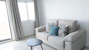 A modern living room with a sofa, a round ottoman, and a window with curtains. - Seafront apartment with pool in Benalmádena (Benalmádena)