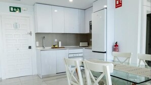 A modern kitchen with white cabinets, a glass dining table, and white chairs. - Seafront apartment with pool in Benalmádena (Benalmádena)