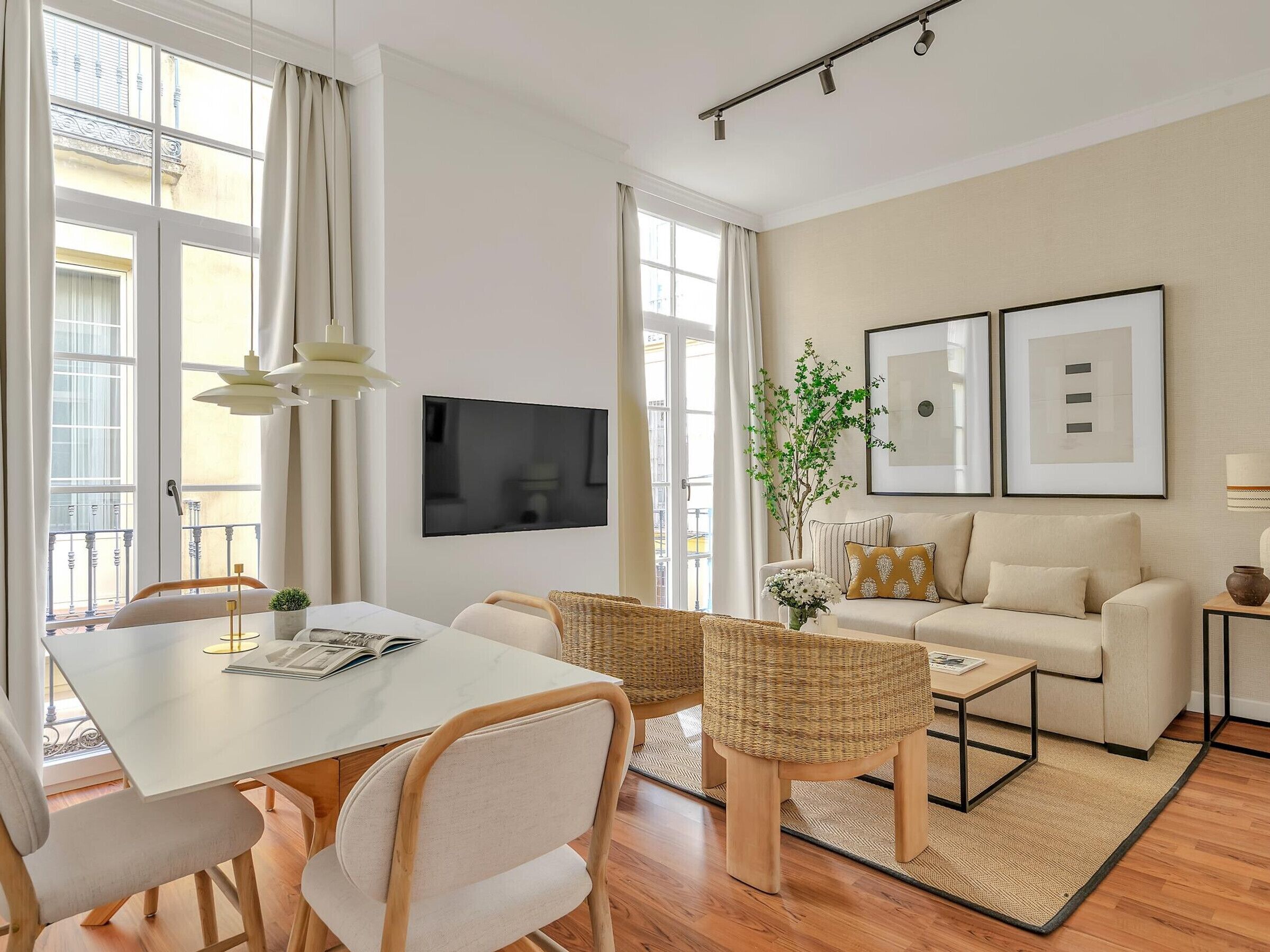 A modern living room with a dining area, a sofa, a TV, and framed artwork.