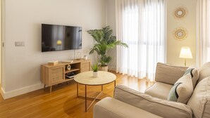 Una sala de estar con una televisión de pantalla plana, una mesa de centro redonda, un sofá, una planta en maceta y una lámpara.