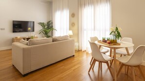 Una sala de estar moderna con un sofá, una mesa de comedor con sillas, un televisor y una planta.