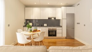 Una cocina moderna con gabinetes blancos, un refrigerador de acero inoxidable y un comedor con mesa y sillas.