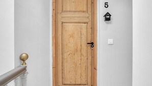 Eine Holztür mit Messingknauf, eine weiße Wand mit der Nummer 5 und ein kleiner schwarzer Briefkasten.