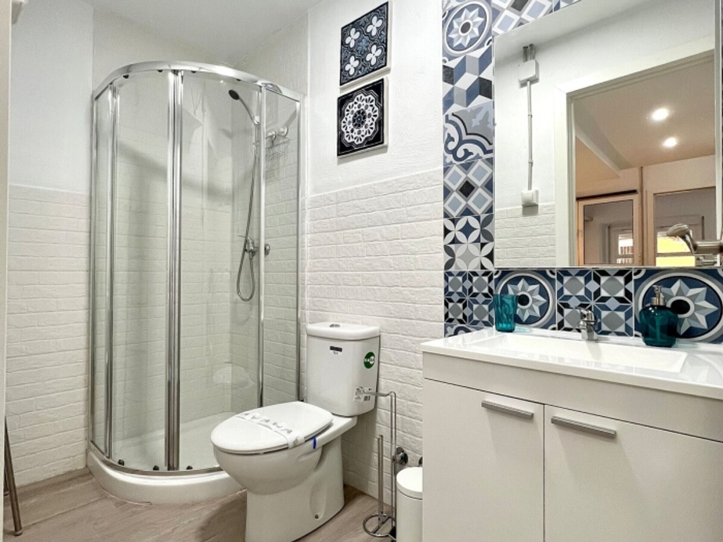 A bathroom with a glass-enclosed shower, a toilet, and a sink with a mirror above it.