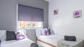 Une chambre avec deux lits, une fenêtre avec un store et deux tableaux représentant des fleurs, accrochés au mur.