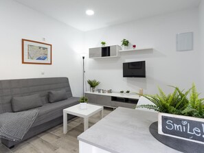 A modern living room with a grey sofa, a coffee table, a flat-screen TV mounted on the wall, and a small shelf with plants. - Modern Apartment near Malaga Beaches (Málaga)