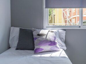 A bed with two pillows, one plain and one with a leaf pattern, in a room with a window and a view of buildings. - Modern Apartment near Malaga Beaches (Málaga)