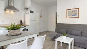 Une cuisine moderne équipée d’un lave-linge intégré, d’un canapé gris et d’une petite table agrémentée d’une plante.