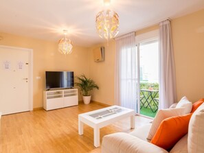 A living room with a TV, a white coffee table, a sofa with orange cushions, a potted plant, and a balcony with a view. - Bright apartment in the heart of Málaga (Málaga)