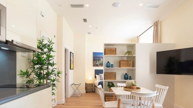 A modern kitchen with a built-in stove, a dining area with white chairs and a table, and a TV mounted on the wall. - Charming apartment near La Malagueta, Malaga (Málaga)