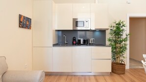 A compact kitchen with white cabinets, a microwave, a kettle, and a small sink. There's a plant in a basket and a beige sofa in the living area. - Charming apartment near La Malagueta, Malaga (Málaga)