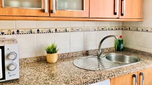 A kitchen with granite countertops, a stainless steel sink, wooden cabinets with glass doors, and a small potted plant. - Spacious apartment with balcony in Málaga (Málaga)