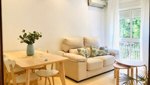A living room with a beige sofa, a dining table with chairs, a small round table, and a potted plant. - Spacious apartment with balcony in Málaga (Málaga)