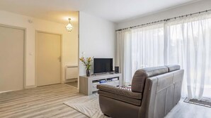 A modern living room with a leather sofa, a flat-screen TV, and a large window with sheer curtains. - Nice home in Saint-Yvi with WiFi (Saint-Yvi)