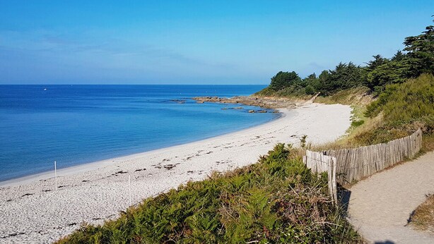 A sandy beach with a wooden fence and greenery, leading to a rocky shoreline. - Nice home in Saint-Yvi with WiFi (Saint-Yvi)